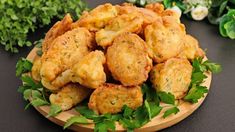 some fried food on a wooden plate with parsley around it and flowers in the background