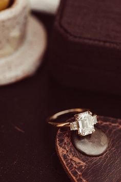 an engagement ring sitting on top of a piece of wood next to a cup and saucer