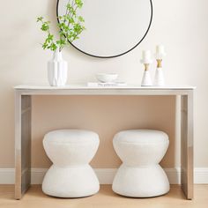 two white stools sitting under a round mirror on a wall next to a table