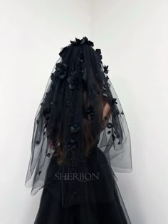 the back of a woman wearing a black dress with flowers on it and veil over her head