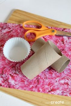 some toilet paper rolls and scissors on a cutting board with pink peonie flowers