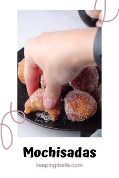 a person reaching for some sugared donuts on a black plate with the words mochisadas