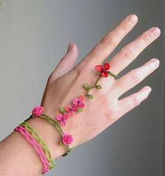 a woman's hand wearing a bracelet with pink flowers on it and green string