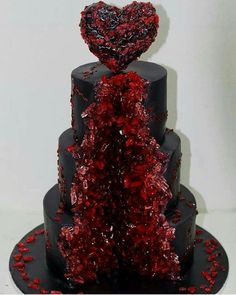 a three tiered cake with red and black decorations on the top, topped with a heart - shaped frosting