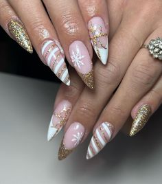 These stiletto nails feature a nude base with gold glitter tips and delicate white snowflake accents. The glitter adds a festive sparkle, while the snowflake design captures the winter feel. This look is perfect for those seeking long and glamorous winter nails. Holiday Nails White And Gold, Gold And White Glitter Nails, Christmas Nails Acrylic Gold, White Gold Holiday Nails, White Gold Winter Nails, Winter Nail Ideas Stiletto, Gold December Nails, Christmas Nails Short Stiletto, Long Nail Christmas Design