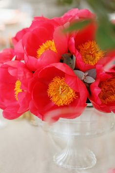 red and yellow flowers are in a clear glass vase on a white tableclothed surface