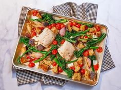 a pan filled with chicken and vegetables on top of a table next to napkins