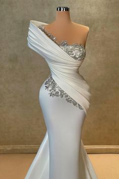 a white dress with silver beading on the shoulders and one shoulder is draped over