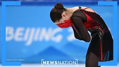 a woman in black and red is bent over with her hands behind her head as she stands on the ice