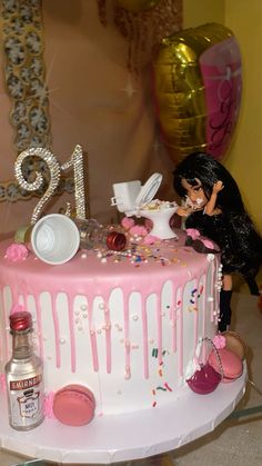 a pink and white birthday cake with a doll on the top, surrounded by confetti