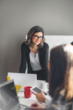 two women sitting at a table with laptops and coffee mugs in front of them