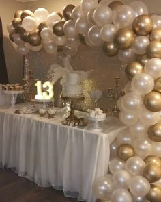 a table topped with lots of white and gold balloons next to a cake on top of a table