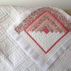 a quilted table runner with pink and white designs on it, sitting on a wooden surface