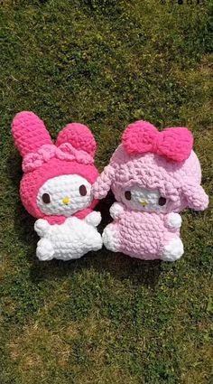 two knitted hello kitty dolls sitting on top of the grass in front of each other