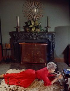 an older woman laying on the floor in front of a fire place