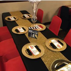 a table set up with gold plates and black napkins for movie themed dinnerware