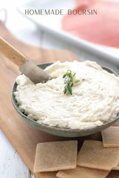 a bowl filled with hummus and crackers on top of a cutting board