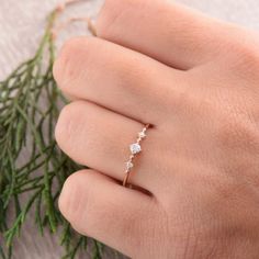 a woman's hand with a ring on top of her finger and some branches in the background