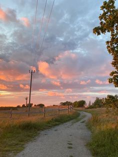 a dirt road with power lines in the distance and clouds in the sky at sunset