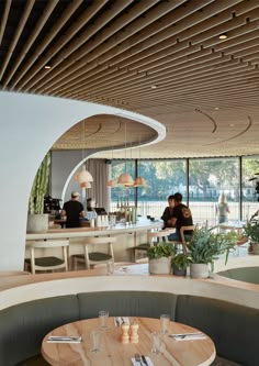 people sitting at tables in a restaurant with lots of windows and plants on the counter