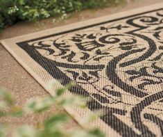 a black and white patterned rug sitting on the ground next to some green plants in front of a bush