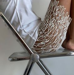 a woman sitting on top of a metal chair with her legs crossed in the air