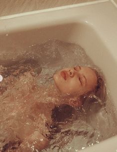 a woman is in the bathtub with her head above the water and eyes closed