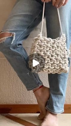 a woman is holding a white purse with chains on the handles and bottom, while wearing ripped jeans