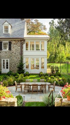 an outdoor dining area in front of a large house with stone walls and white trim