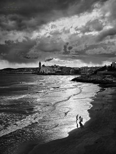 black and white photograph of people walking on the beach in front of an overcast sky