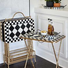 a black and white checkered tray with drinks on it next to a gold serving table