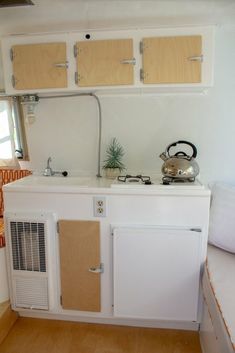 a kitchen with a tea kettle on the stove and cupboards over the sink area