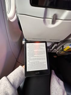 a kindle sitting on top of a seat next to a book shelf in an airplane