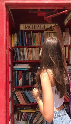 a woman is standing in a red phone booth with bookshelves full of books