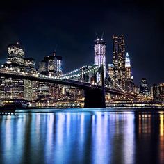 the city skyline is lit up at night with lights reflecting on the water and skyscrapers in the background