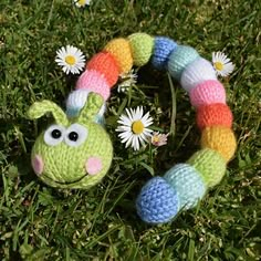 a crocheted caterpillar toy laying in the grass with daisies