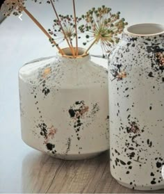 two white vases with splattered black and gold designs on them sitting on a table