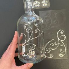 a hand is holding a crystal decal next to a glass bottle with an ornate design on it