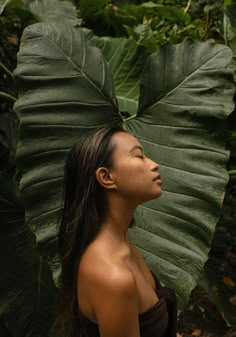 a woman standing in front of a large leaf with her head turned to the side