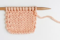 the knitting needle is next to an orange piece of yarn that has been knitted