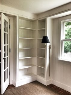 an empty room with white bookcases and a lamp on the floor next to it