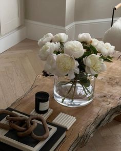 white flowers in a glass vase on a wooden table with books and other items around it