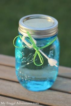 a mason jar filled with blue liquid sitting on top of a wooden table next to grass