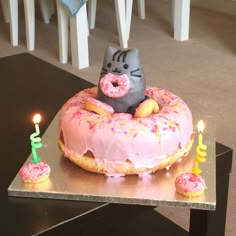 a cat sitting on top of a donut with pink frosting and sprinkles