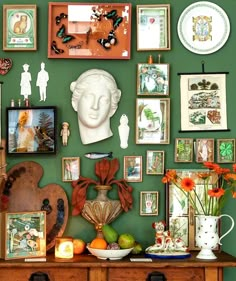 a green wall covered in pictures and framed art on top of a wooden dresser next to a vase filled with flowers