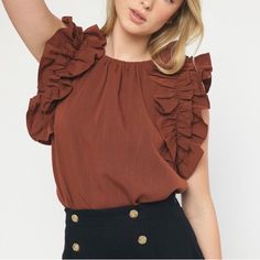 a woman wearing a brown top with ruffles on it's shoulders and black pants