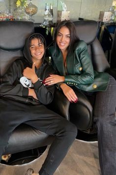 two women sitting in black leather chairs smiling at the camera with their arms around each other