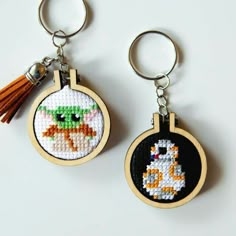 two cross stitch keychains with tassels hanging from them, one has a duck and the other has a cat