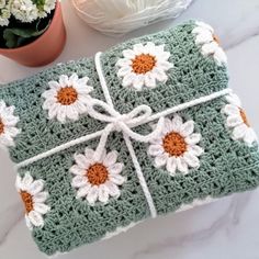 a green crocheted blanket with white and orange flowers on it next to a potted plant