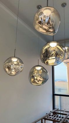 three glass globes hanging from the ceiling above a table and chairs in front of a large window